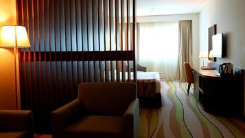 A hotel room with a bed, a desk, a chair, a lamp, and a TV.