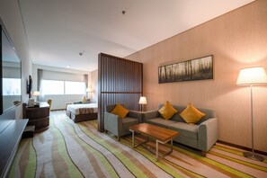 A modern hotel room with a sofa, a coffee table, a TV, and a bed. - Jacob's Garden Hotel (Dubai)