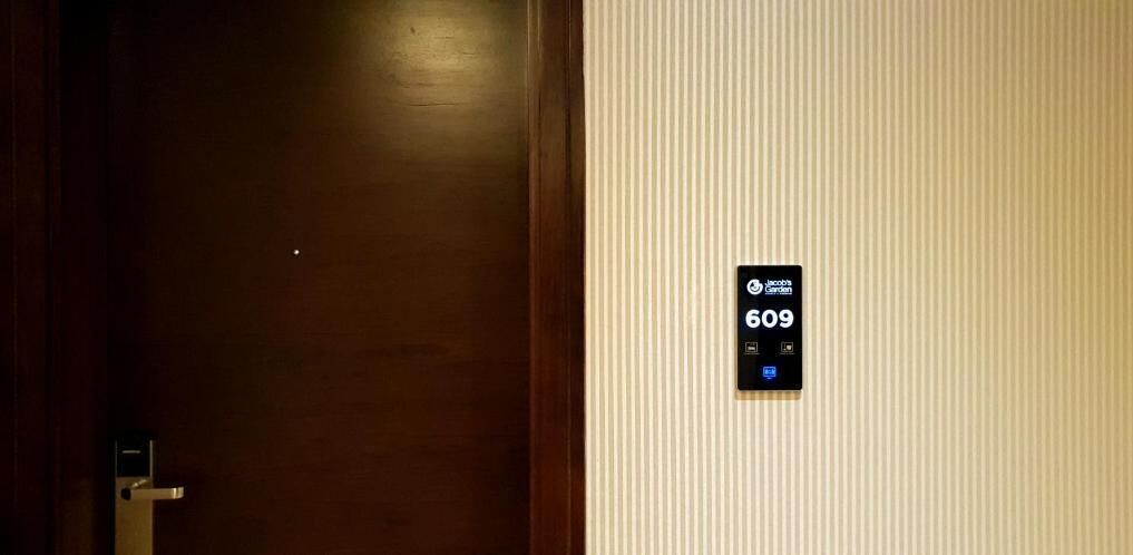 Quarto de hotel com porta de madeira e painel de controle fixado na parede exibindo o número 609.