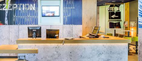 Una mesa de recepción con computadora, televisor y cafetera.