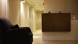 Una moderna zona de recepción con un sillón oscuro, un mostrador de madera y un ordenador portátil sobre el mostrador.