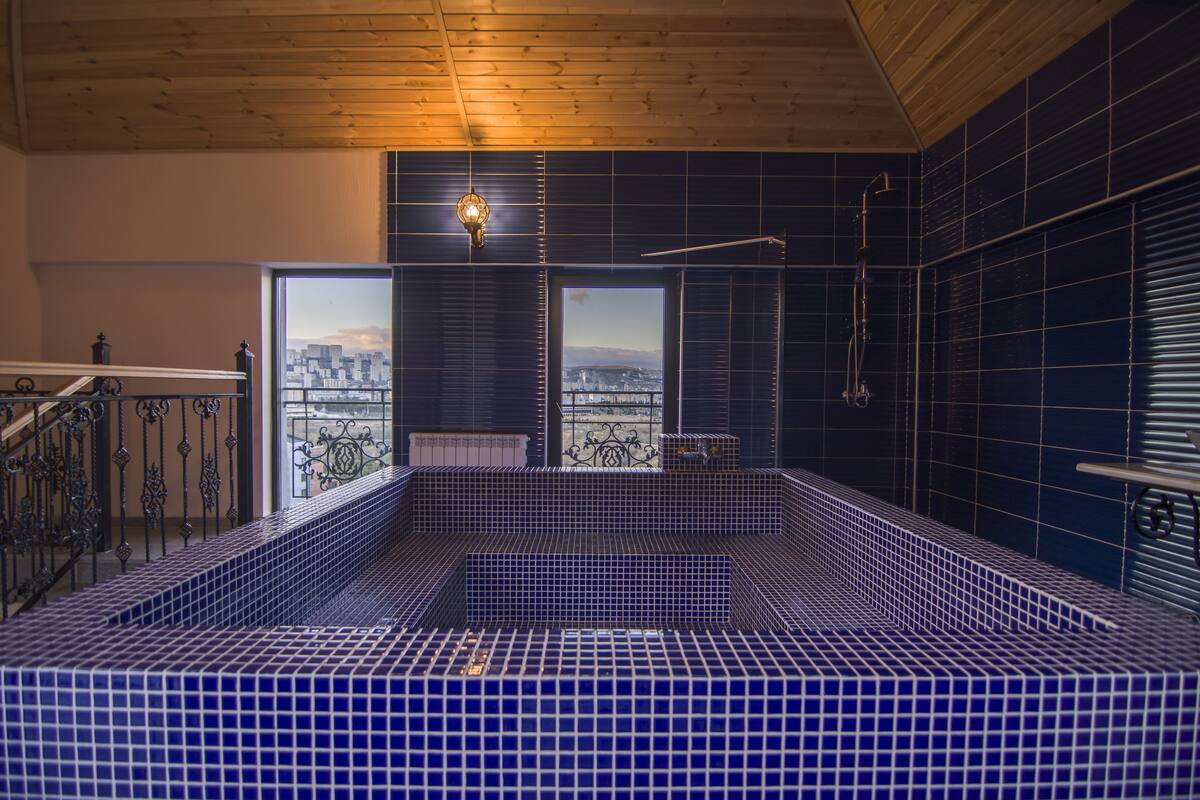 Un jacuzzi aux carreaux bleus offrant une vue sur la ville, avec un plafond en bois et une balustrade.