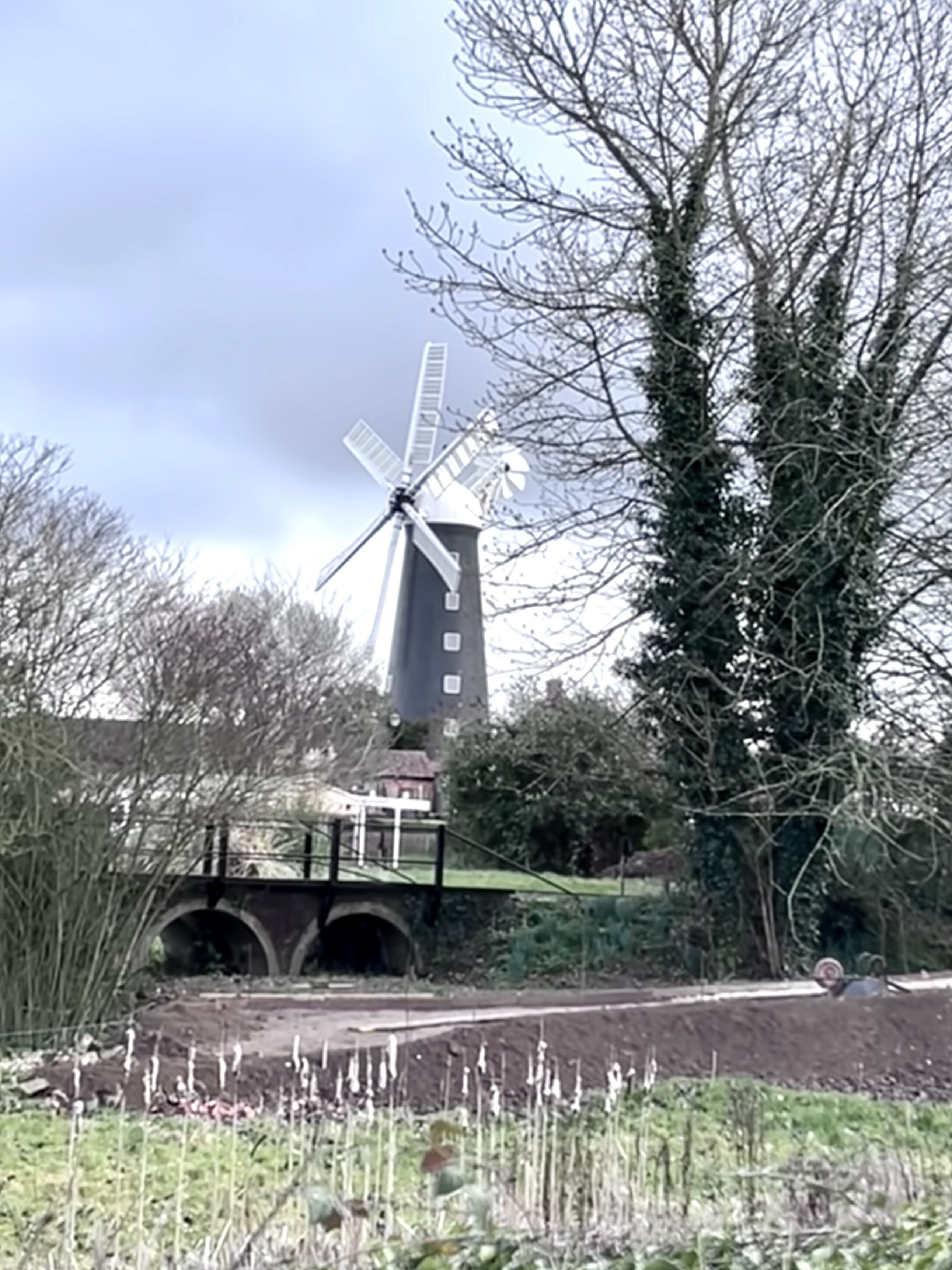 Un moulin à vent, avec un pont au premier plan et des arbres en arrière-plan.