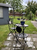 A patio with a metal table and chairs, surrounded by a grassy yard and a wooden fence.