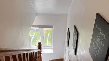 A staircase with a wooden railing, a window with a view of greenery, and a wall with framed pictures and a chalkboard with text.