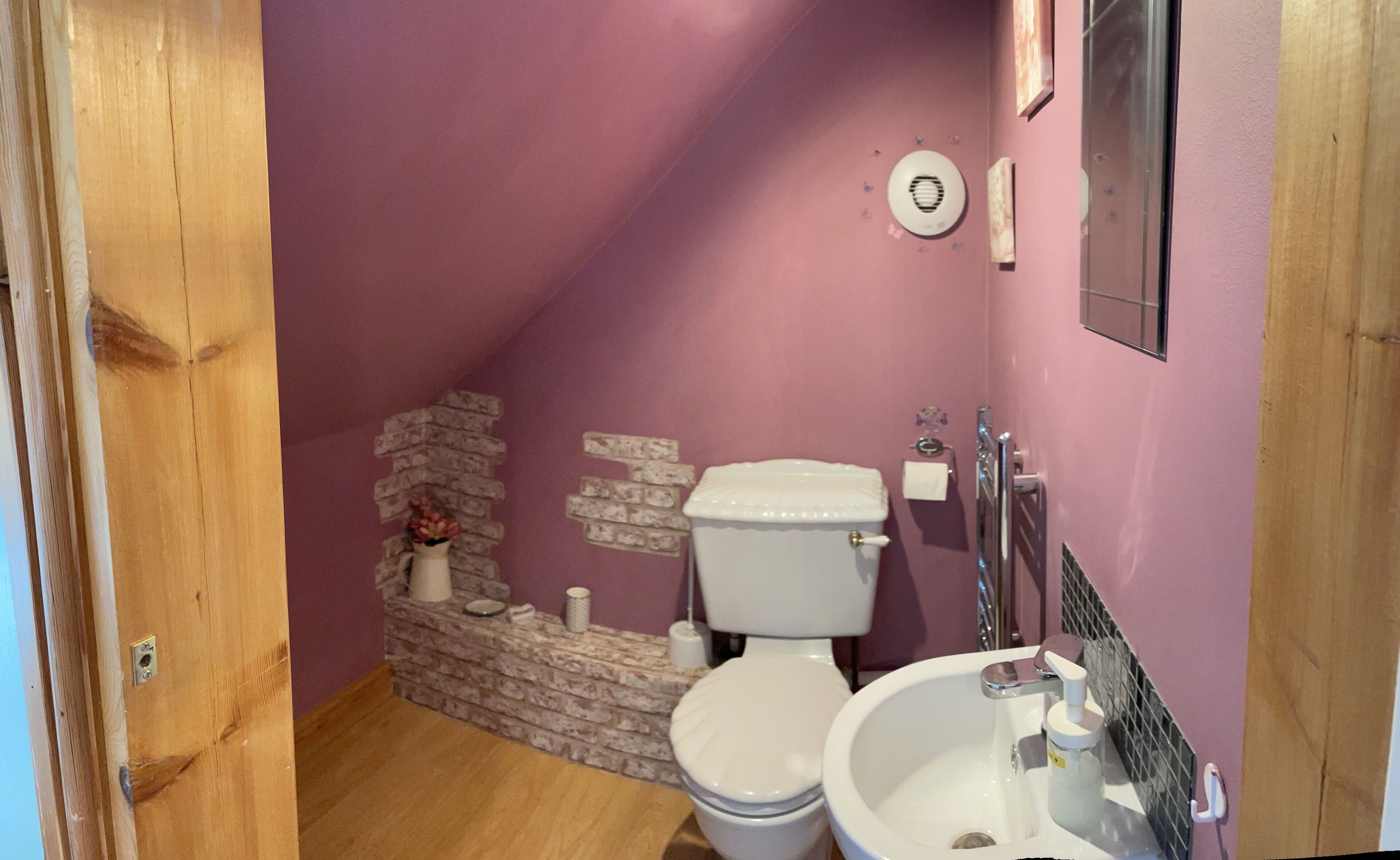 Een badkamer met een paarse muur, een wit toilet en een wastafel met een spiegel erboven.
