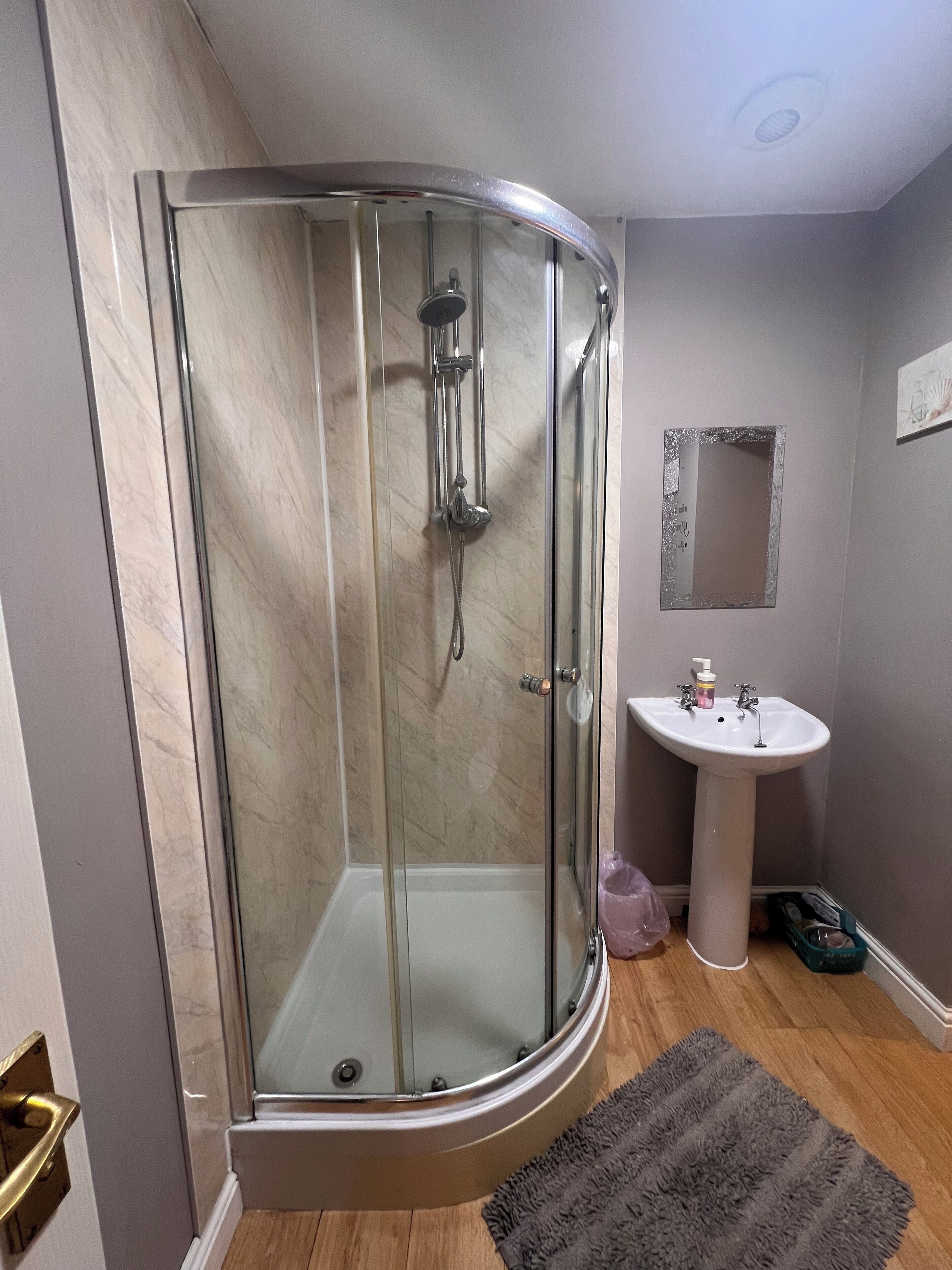 Ducha envuelta en vidrio con cabezal de ducha de mano y llave de pared.