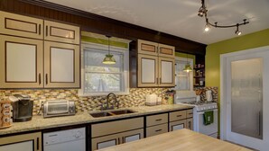 A kitchen with wooden cabinets, a granite countertop, a dishwasher, a stove, and a window with blinds. - Cottage by the Historic Depot (Boise)