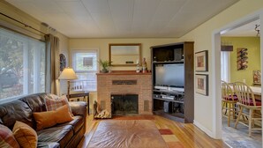 A living room with a fireplace, a sofa, a TV, and a dining area with chairs. - Cottage by the Historic Depot (Boise)