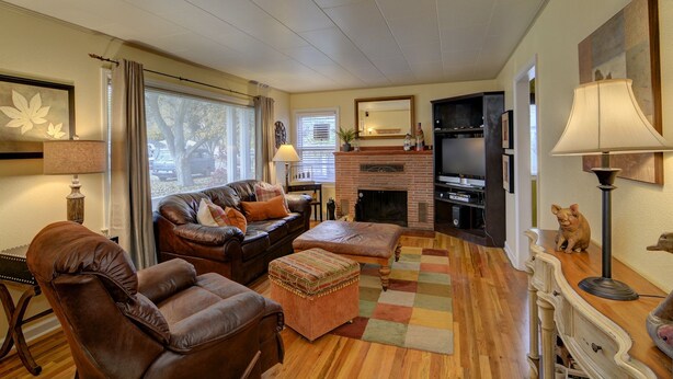 A cozy living room with a leather sofa, a fireplace, a television, and a dog statue. - Cottage by the Historic Depot (Boise)