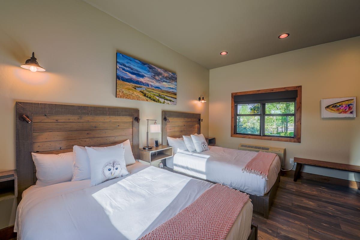 A hotel room with two beds, wooden headboards, a large window, and a painting on the wall.