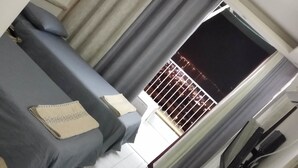 A room with a bed, a window with curtains, and a view of a building outside. - Migdaley Nof Hamifraz (Eilat)