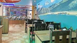 A restaurant with a mural of a mountainous landscape and a lake. Tables and chairs are arranged for dining. - Hotel Readers Inn Pvt.Ltd (Kathmandu)
