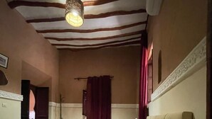 A bedroom with a bed, a hanging light fixture, a door, and a window with curtains. - Dar Boumida (Lalla Takarkoust)