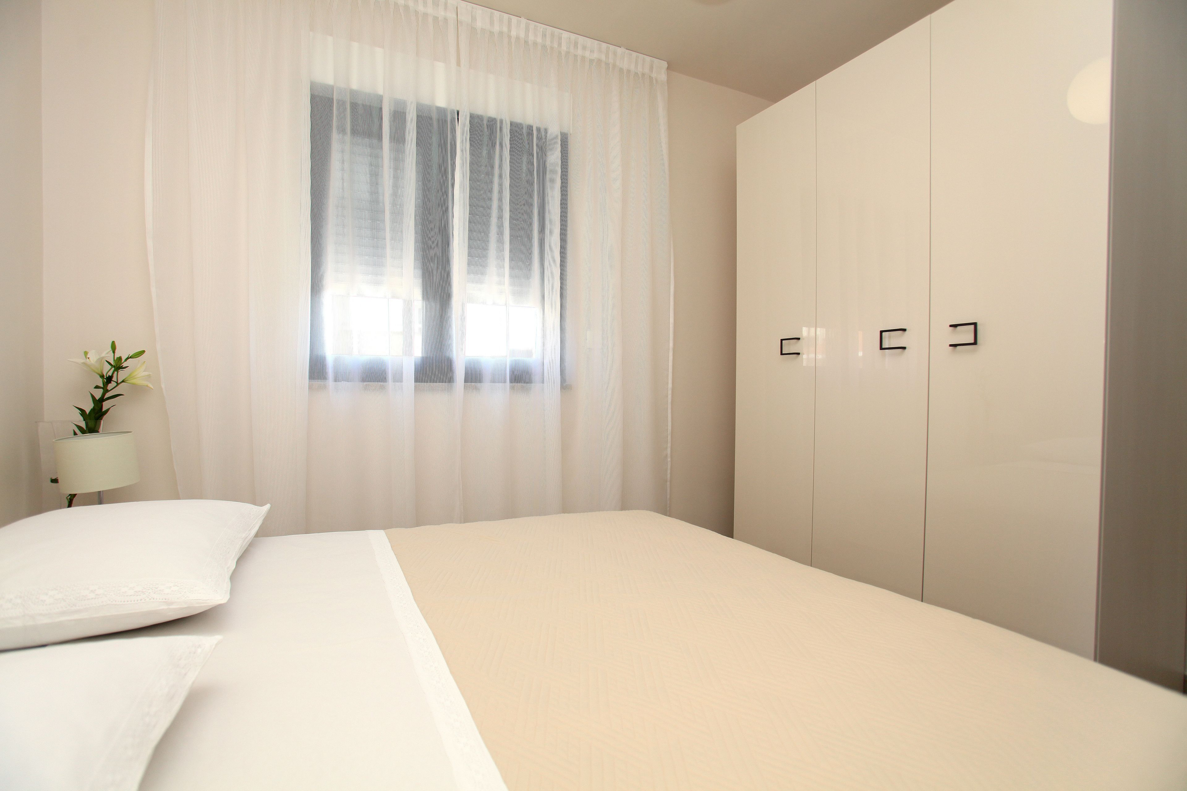 Una camera da letto con un letto grande, una finestra con tende leggere, una lampada da comodino e un armadio.