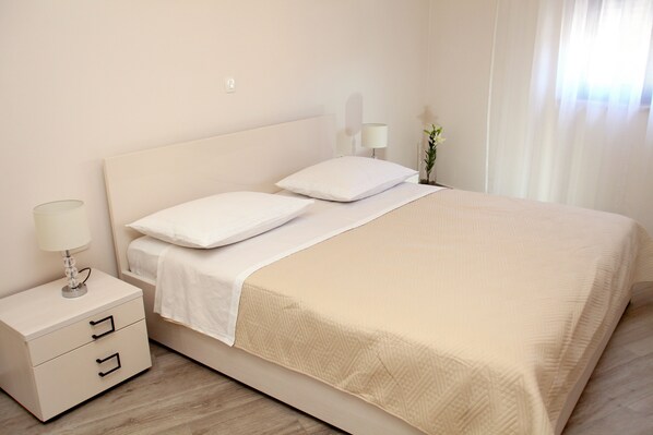 A neatly made bed with a white headboard, a bedside table with a lamp, and a small potted plant. - Villa Aquamarie (Trogir)