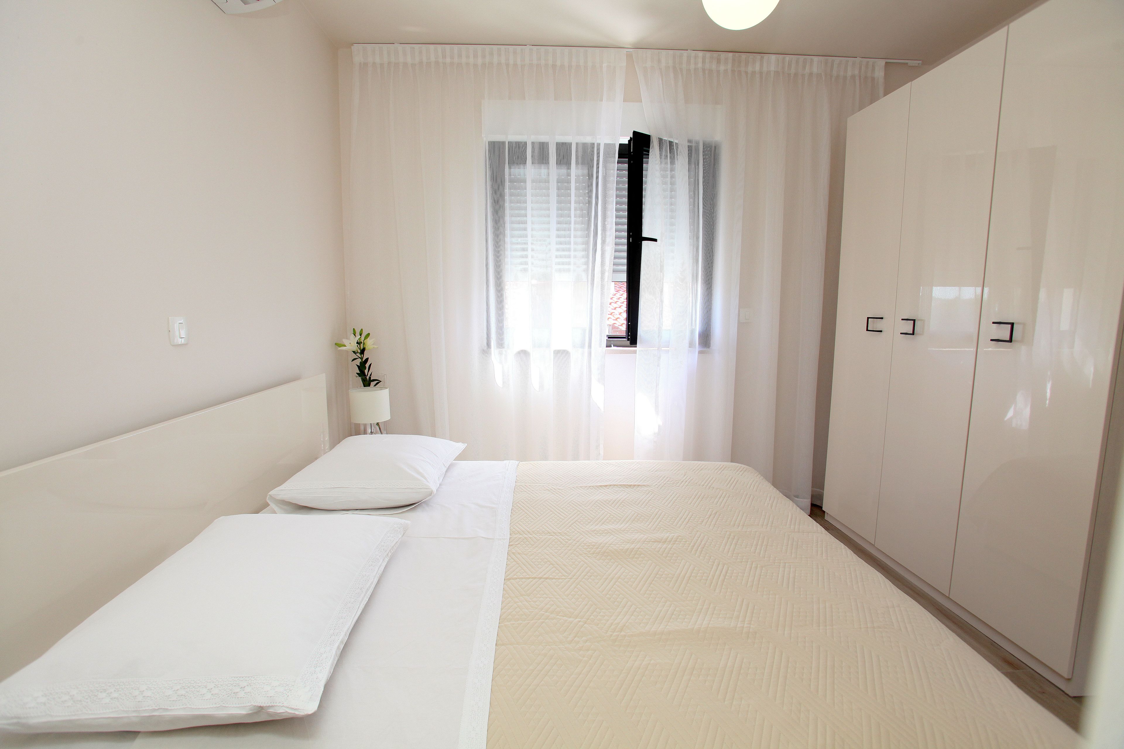 A bedroom with a bed, a wardrobe, and a window with sheer curtains.