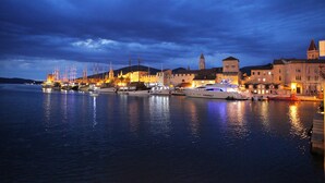 A waterfront marina at dusk with boats docked, historic buildings, and a prominent tower. - Villa Aquamarie (Trogir)