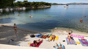 A beach with people sunbathing and swimming, boats on the water, and a clear sky. - Villa Aquamarie (Trogir)