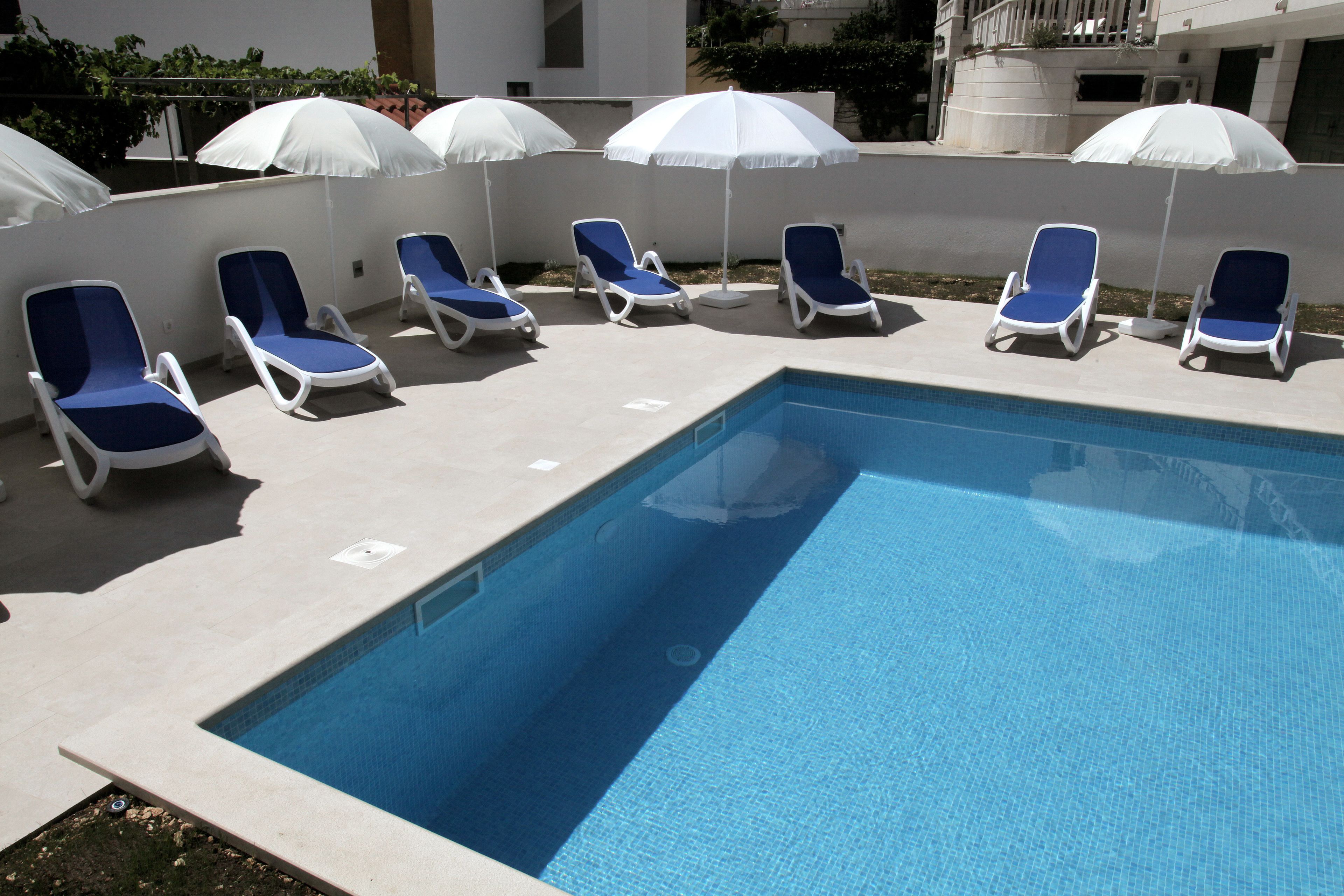 Una piscina con lettini blu e ombrelloni bianchi.