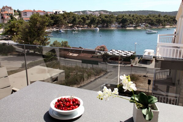 A balcony with a view of a marina, a bowl of cherries, and a potted orchid. - Villa Aquamarie (Trogir)