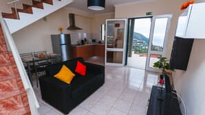 A modern living room with a black sofa, a dining table, and a kitchen area. - Sea View Apartment Single Beds with Swimming Pool (Arco da Calheta)