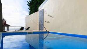 A swimming pool with a clear blue water surface, a metal ladder, and a white wall. - Sea View Apartment Single Beds with Swimming Pool (Arco da Calheta)