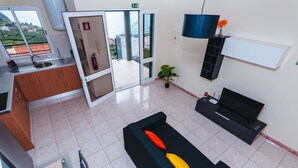 A modern hotel lobby with a kitchen area, a seating area with a black sofa, and a TV stand. - Sea View Apartment Single Beds with Swimming Pool (Arco da Calheta)