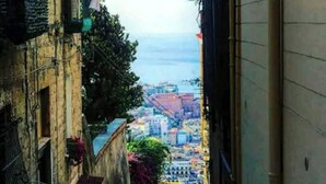 A narrow alleyway with buildings on either side, leading to a view of the sea and cityscape. - V & V (apartment Valentina and Viviana) (Napoli)