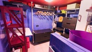 A compact room with a bunk bed, a small desk, a shelf with hanging items, and a purple storage bin. - V & V (apartment Valentina and Viviana) (Napoli)