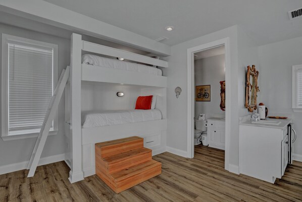 Un dormitorio con una cama litera, una escalera de madera, un armario blanco y un baño visible a través de una puerta abierta.