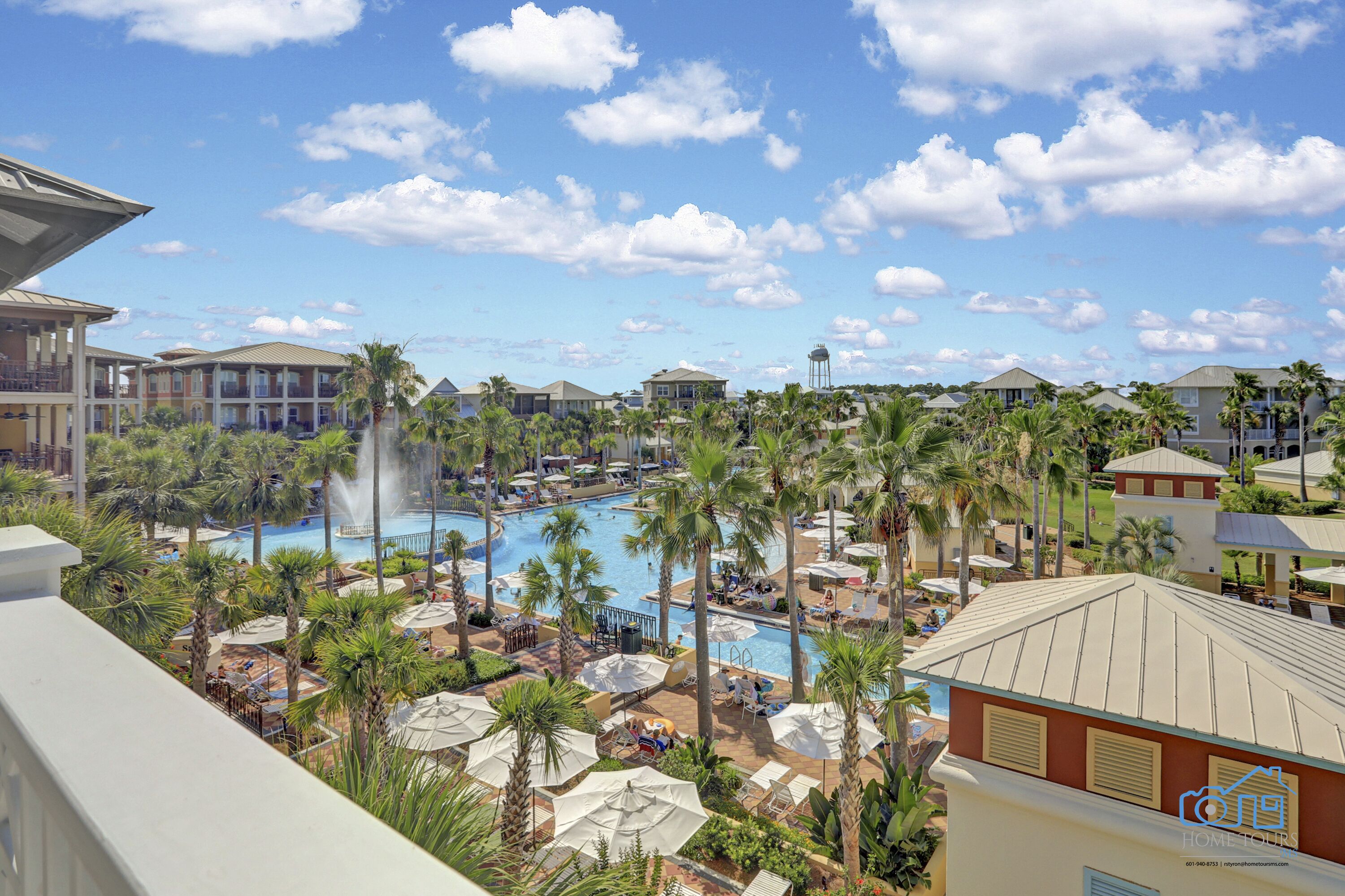 Een resort met een centraal gelegen zwembad, omringd door palmbomen en ligbedden.