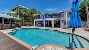 A pool area with a wooden deck, a bar area, and a two-story building with a blue exterior. - Waterfront -Canal, Heated Pool, Tiki Bar, Free 6P Golf Cart Promo Ends 8/31! (Anna Maria)