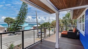 A wooden deck with outdoor furniture, overlooking a beach with houses and a clear sky. - Waterfront -Canal, Heated Pool, Tiki Bar, Free 6P Golf Cart Promo Ends 8/31! (Anna Maria)