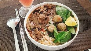 Un verre de smoothie rose et un bol de soupe contenant des boulettes de viande et des légumes, posés sur une table.