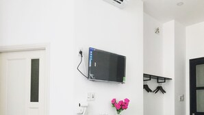 Une chambre d’hôtel avec un bureau noir, un petit réfrigérateur, un téléviseur fixé au mur, un sèche-cheveux, un distributeur d’eau et un vase avec des fleurs.