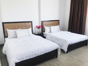 Two single beds with headboards, white bedding, a nightstand with a vase of flowers, and a brown curtain. - Phuc Lam Hotel (Da Nang)