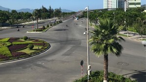 Un carrefour urbain moderne, avec un rond-point central, entouré d’espaces verts bien entretenus et de palmiers.