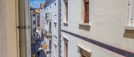 A narrow street with buildings on either side, a clear sky, and a few pedestrians.