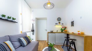 A modern living room with a grey sofa, a small coffee table, and a kitchen area with a wooden countertop and two black stools. - Rijeka Apartments Terra City Center (Rijeka)