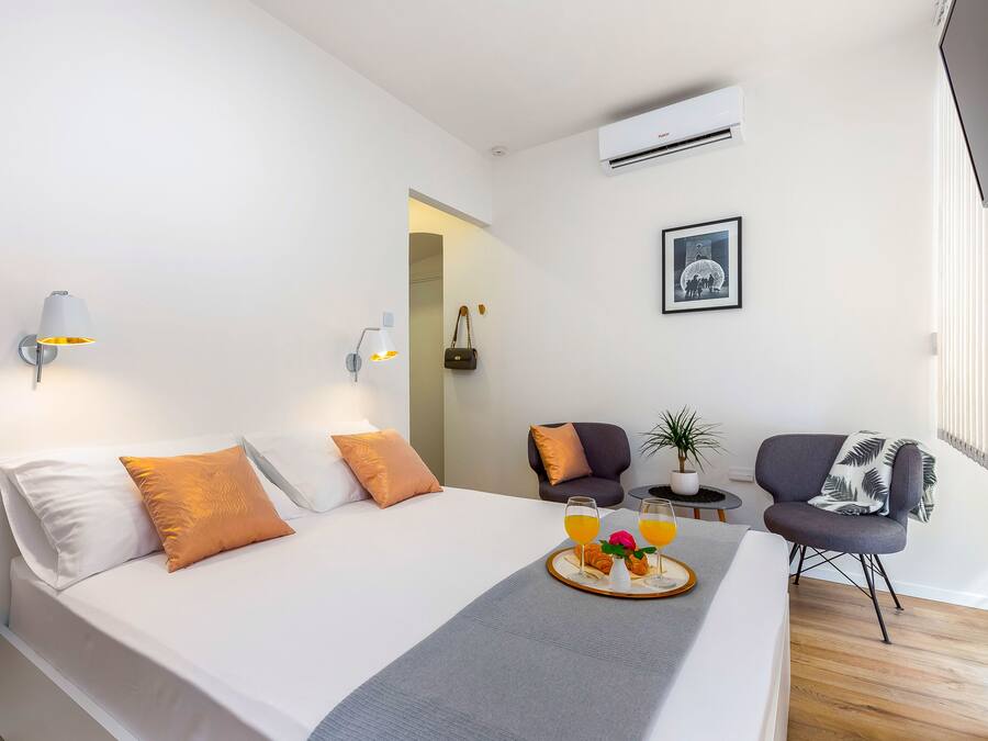 A modern hotel room with a neatly made bed, a bedside table with a tray of breakfast, a chair, and a small table with a plant.