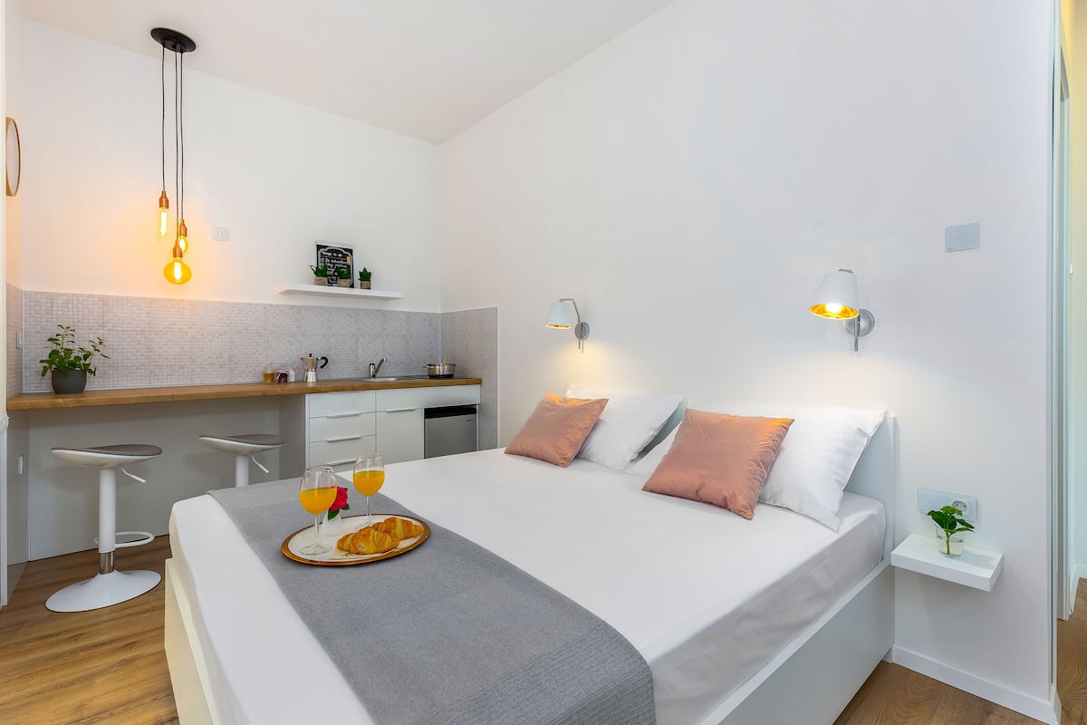 Une chambre moderne comprenant un lit, des tables de chevet, un petit coin cuisine et une table à manger où le petit-déjeuner est servi.
