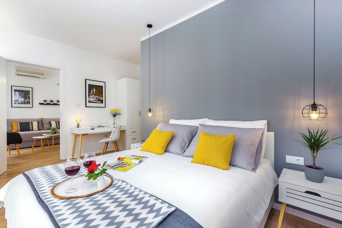 Une chambre d’hôtel moderne avec un grand lit, une table de chevet avec une lampe, un petit bureau et une plante en pot.