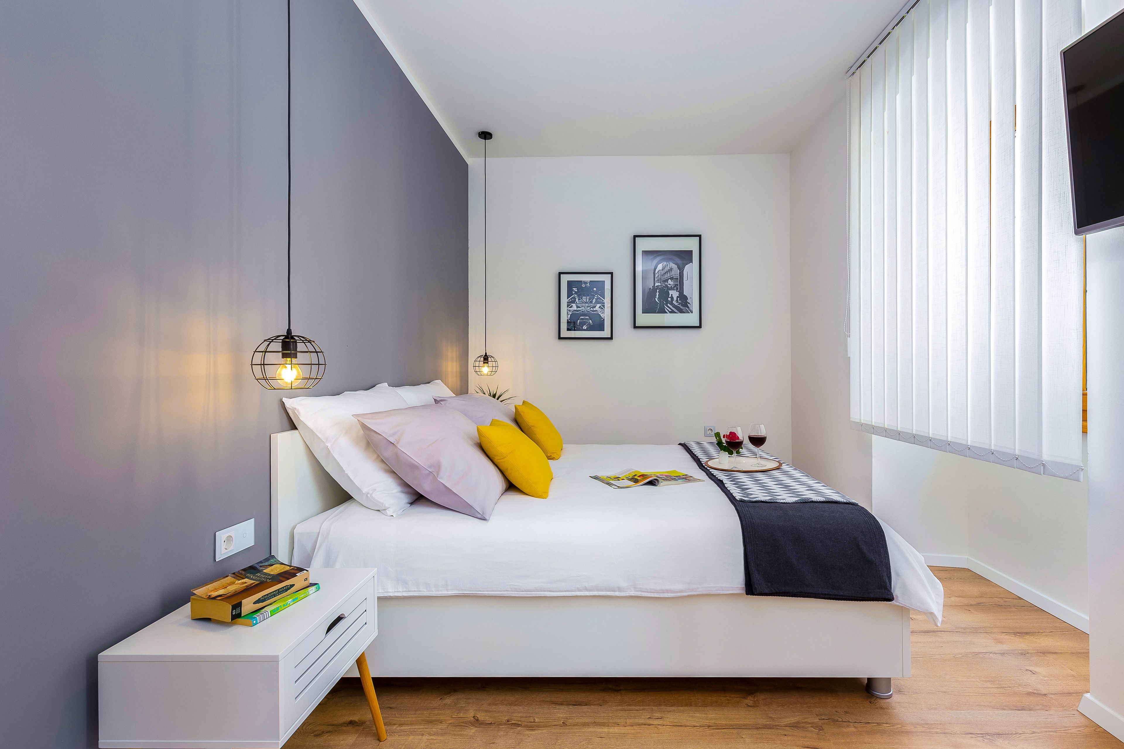 A modern bedroom with a bed, bedside table, and a window with blinds.