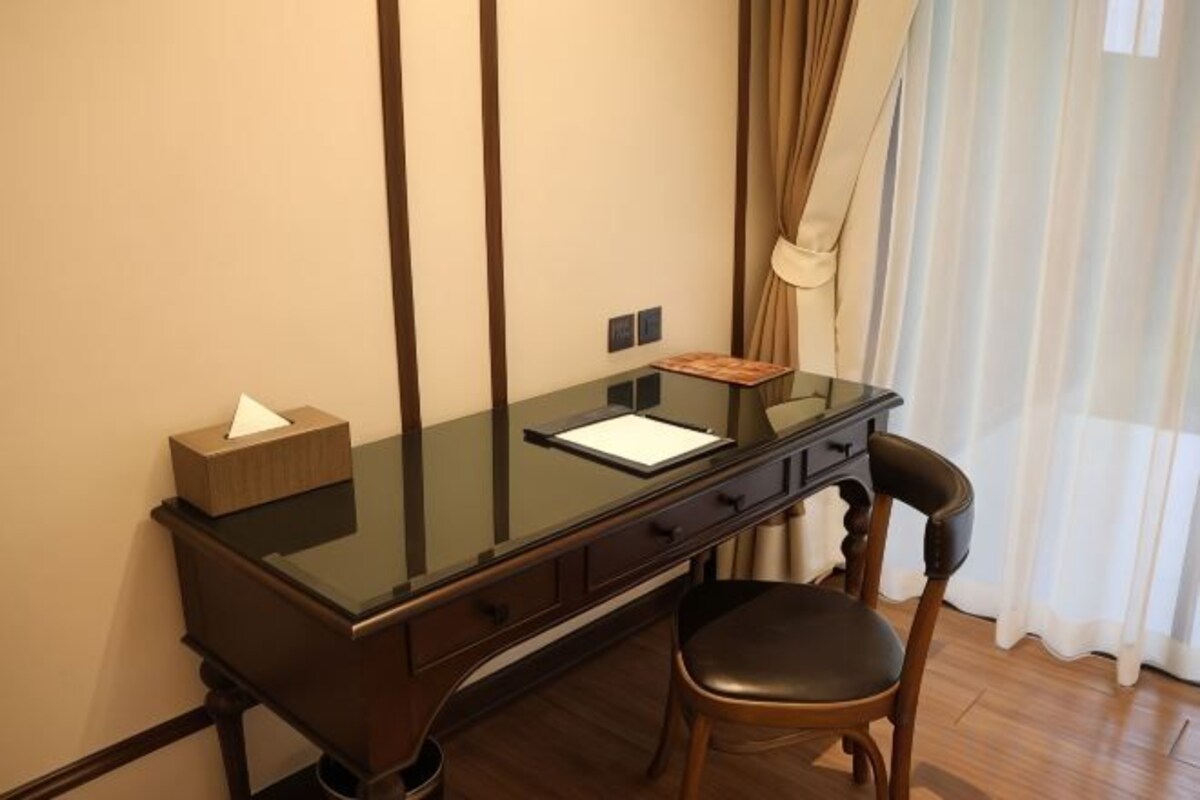 A room with a glass-top desk, a chair, a lamp, and a window with curtains.