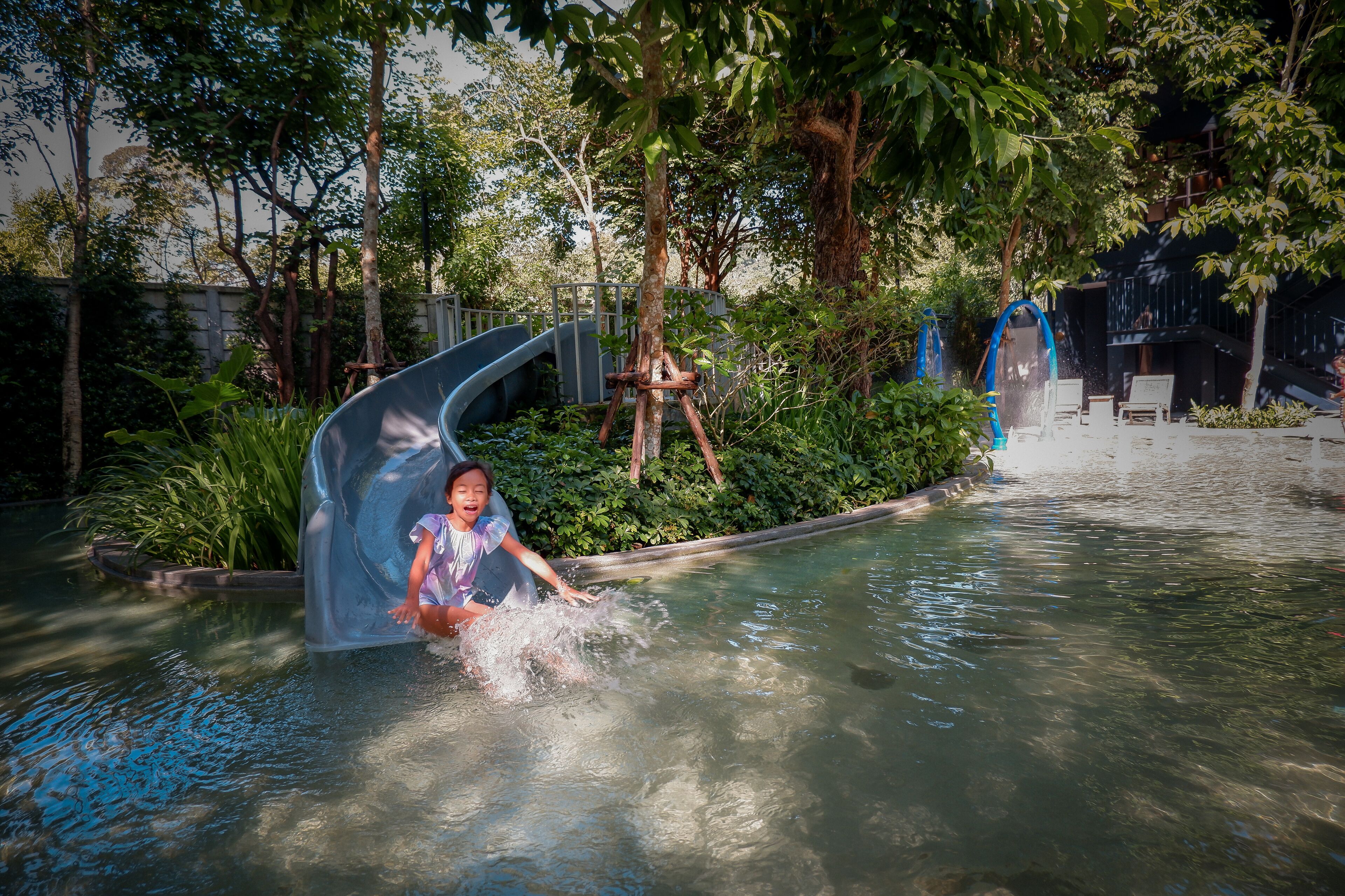 A water play area with a slide and a small pool, surrounded by greenery and trees.