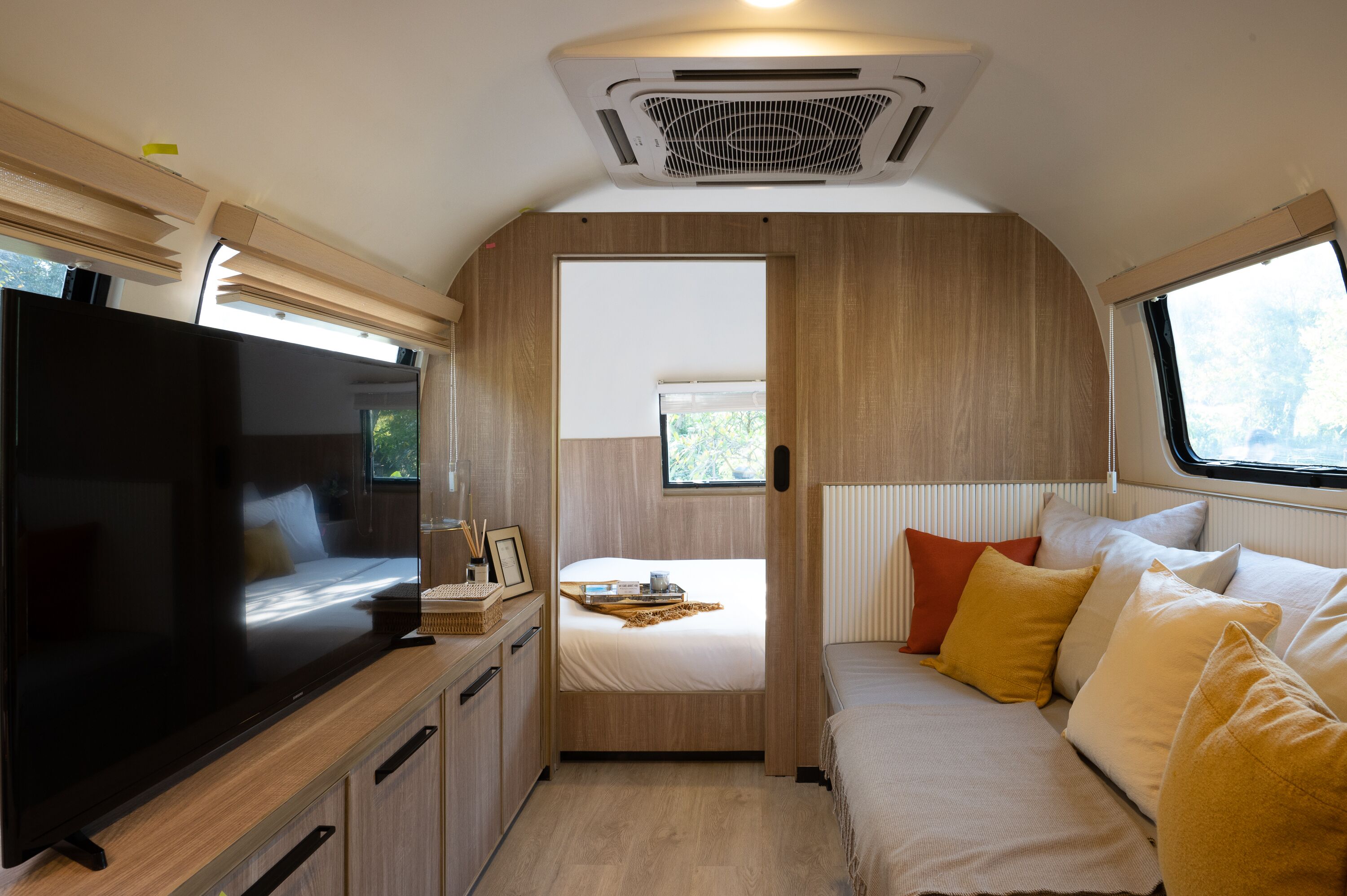 En kompakt autocamper indretning med fjernsyn, seng, lille tekøkken og et vindue med naturligt lys.