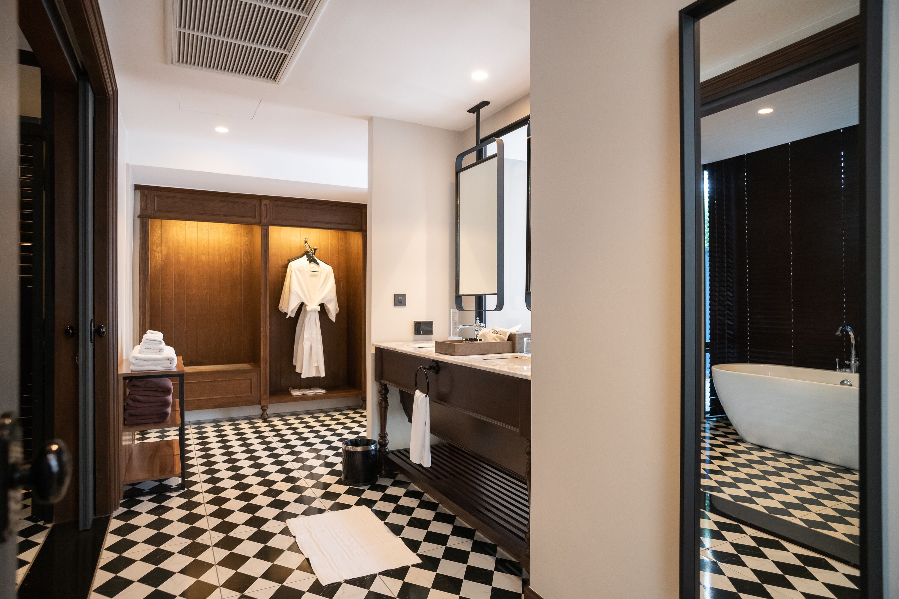 A modern bathroom with a checkered floor, a large bathtub, a vanity with a mirror, and a wooden wardrobe.