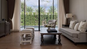 A spacious living room with a large sliding glass door leading to a pool, a sofa, a coffee table, and a chair. - Hotel Labaris Khao Yai (Pak Chong)