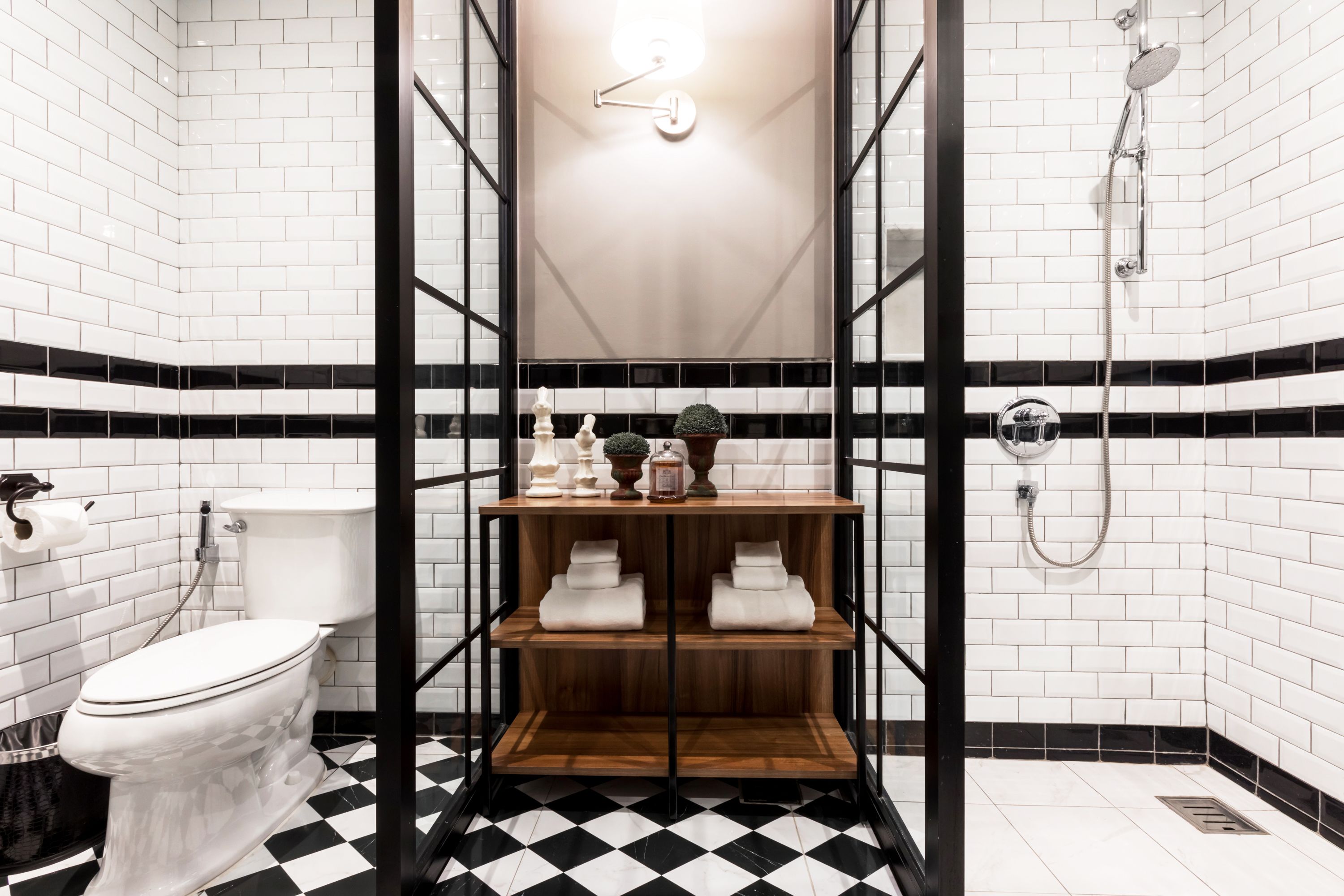 Une salle de bain avec des toilettes, une étagère avec des serviettes, une douche et un carrelage noir et blanc à motifs carrés.